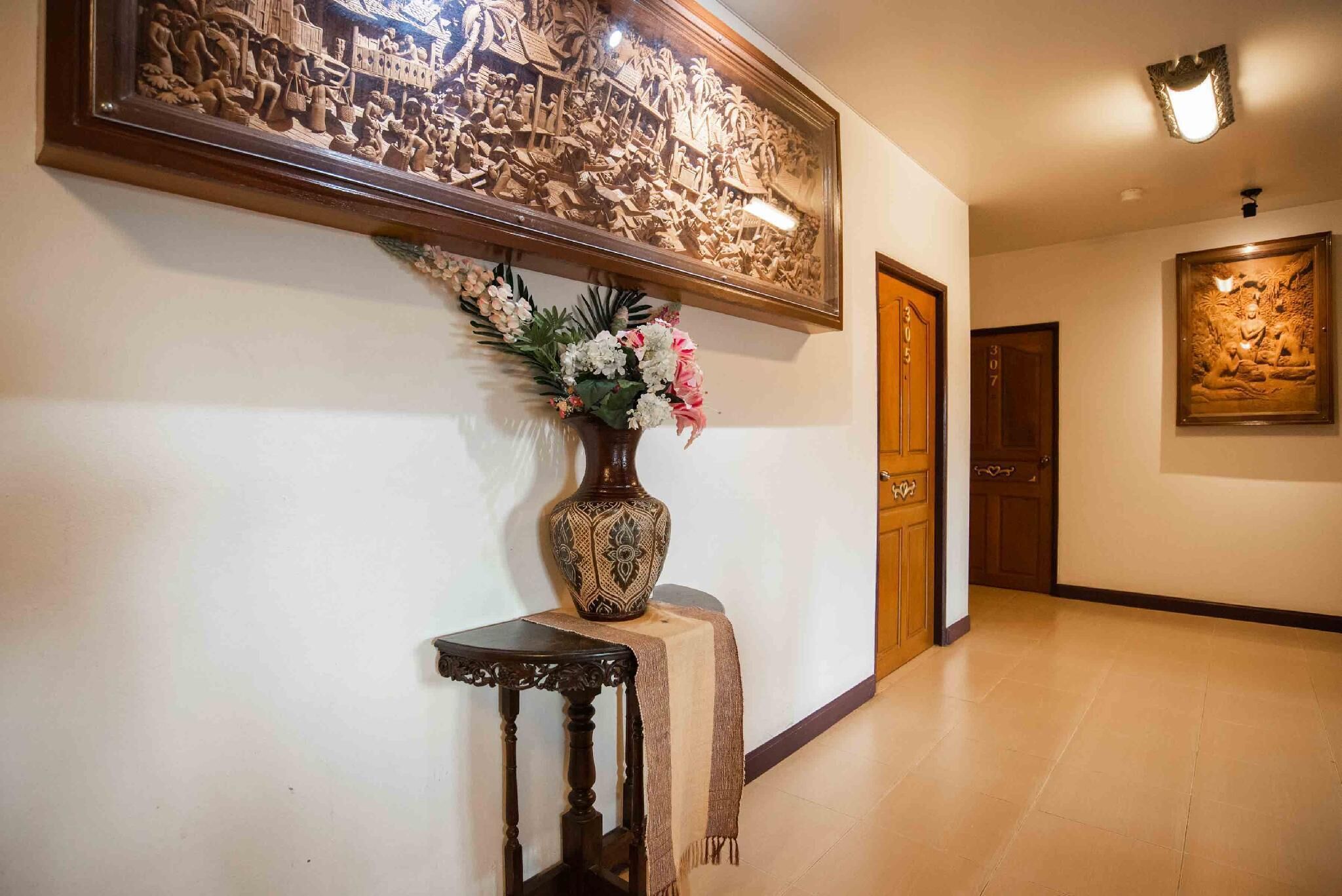 A hallway with a large carved wooden panel above a table with a vase of flowers.