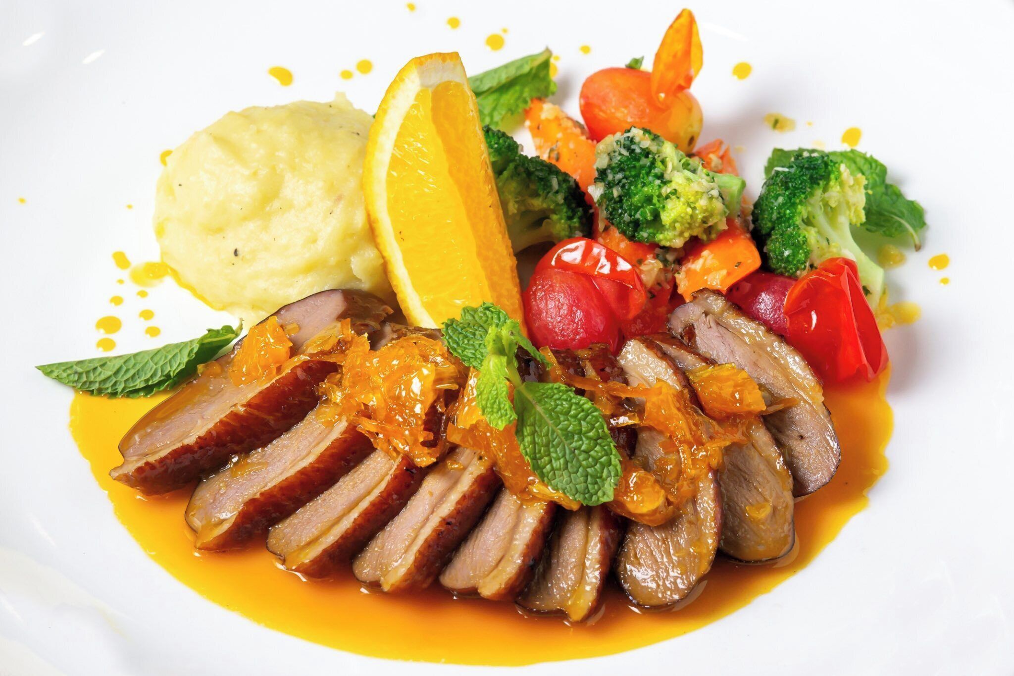A plate of food with sliced duck, vegetables, and a lemon slice.