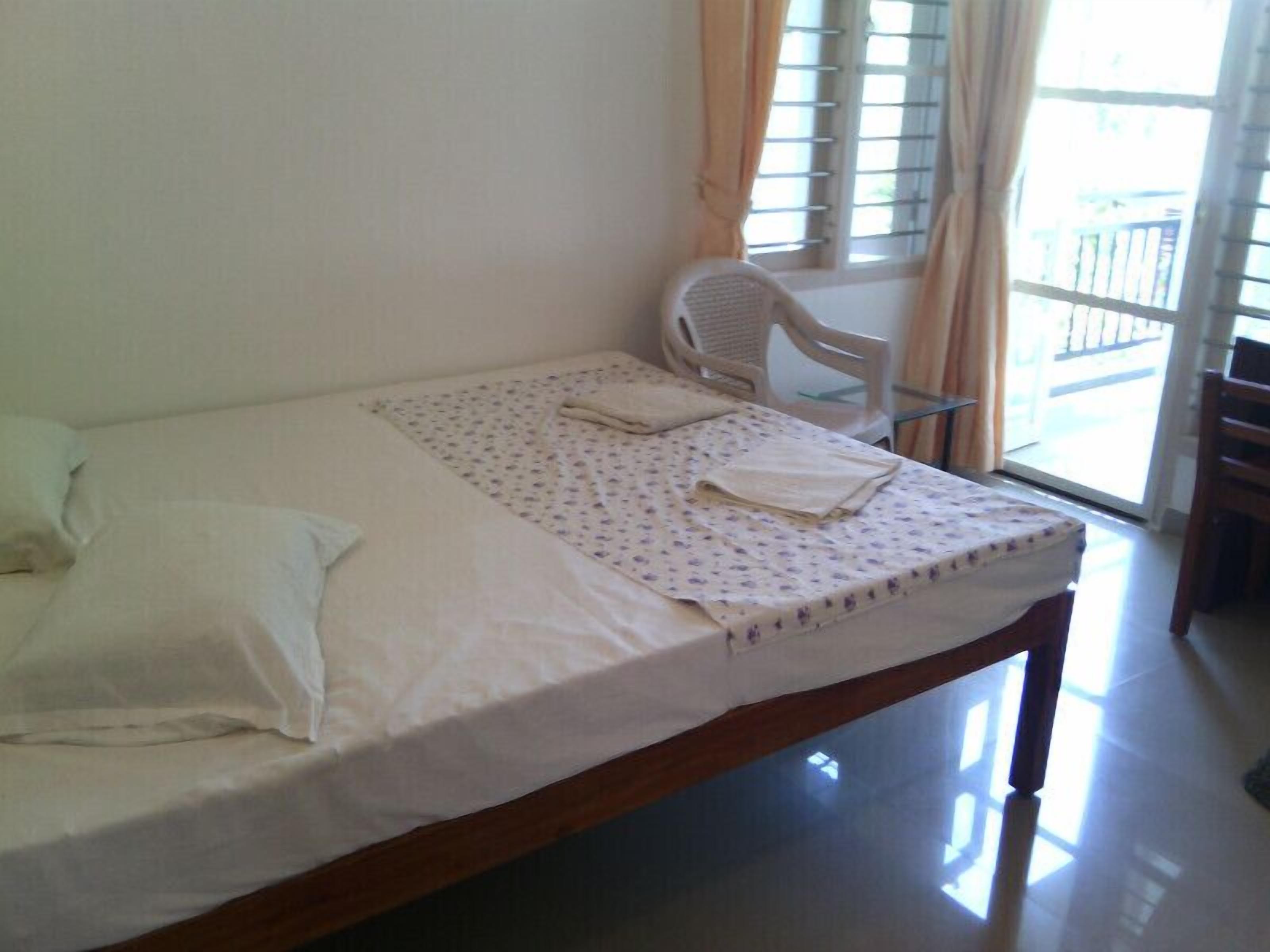 A single bed with a white mattress and a floral-patterned bedspread, a white pillow, and a folded towel on the bed.