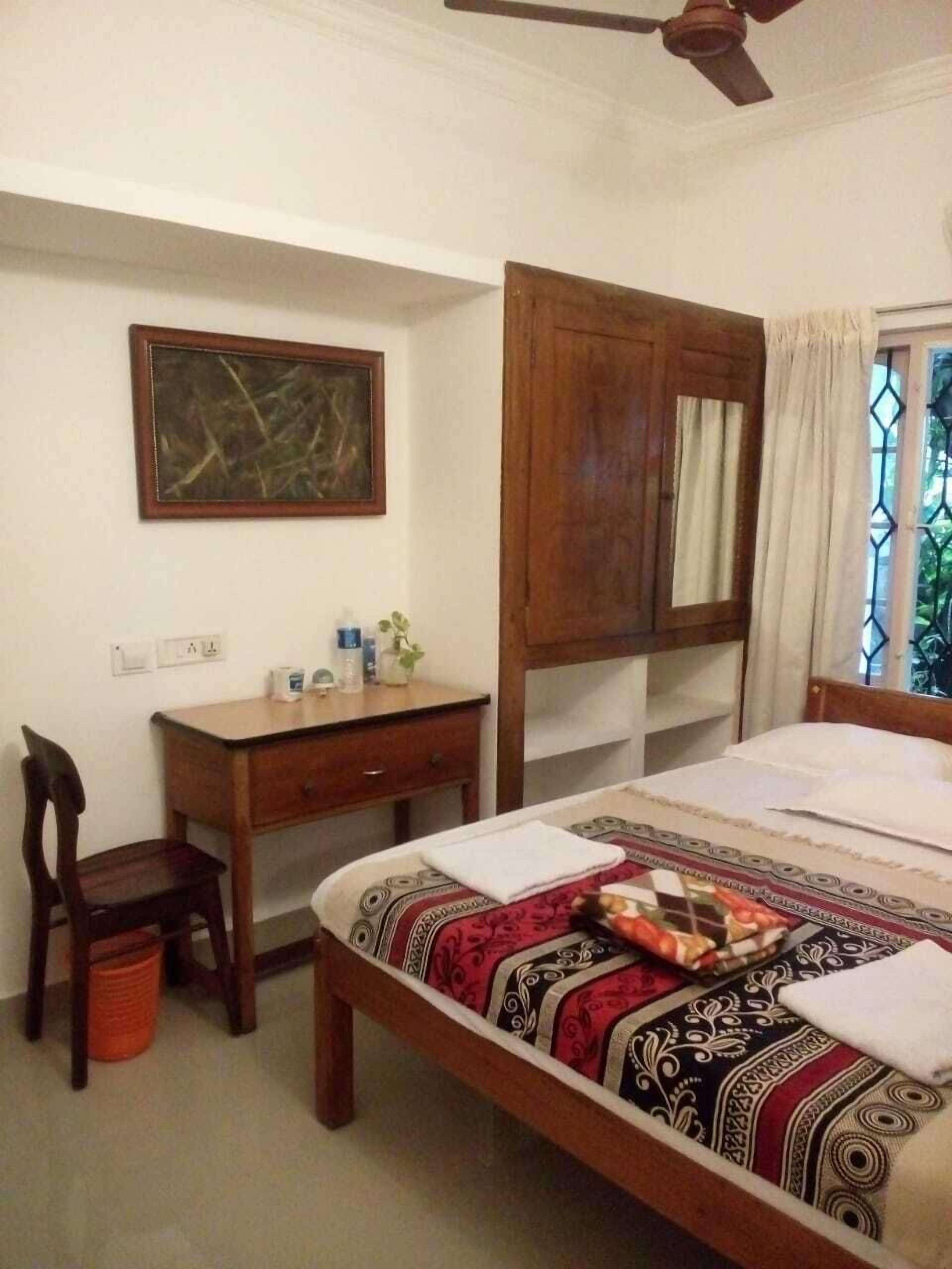 A bedroom with a wooden bed, a desk, a chair, and a ceiling fan.