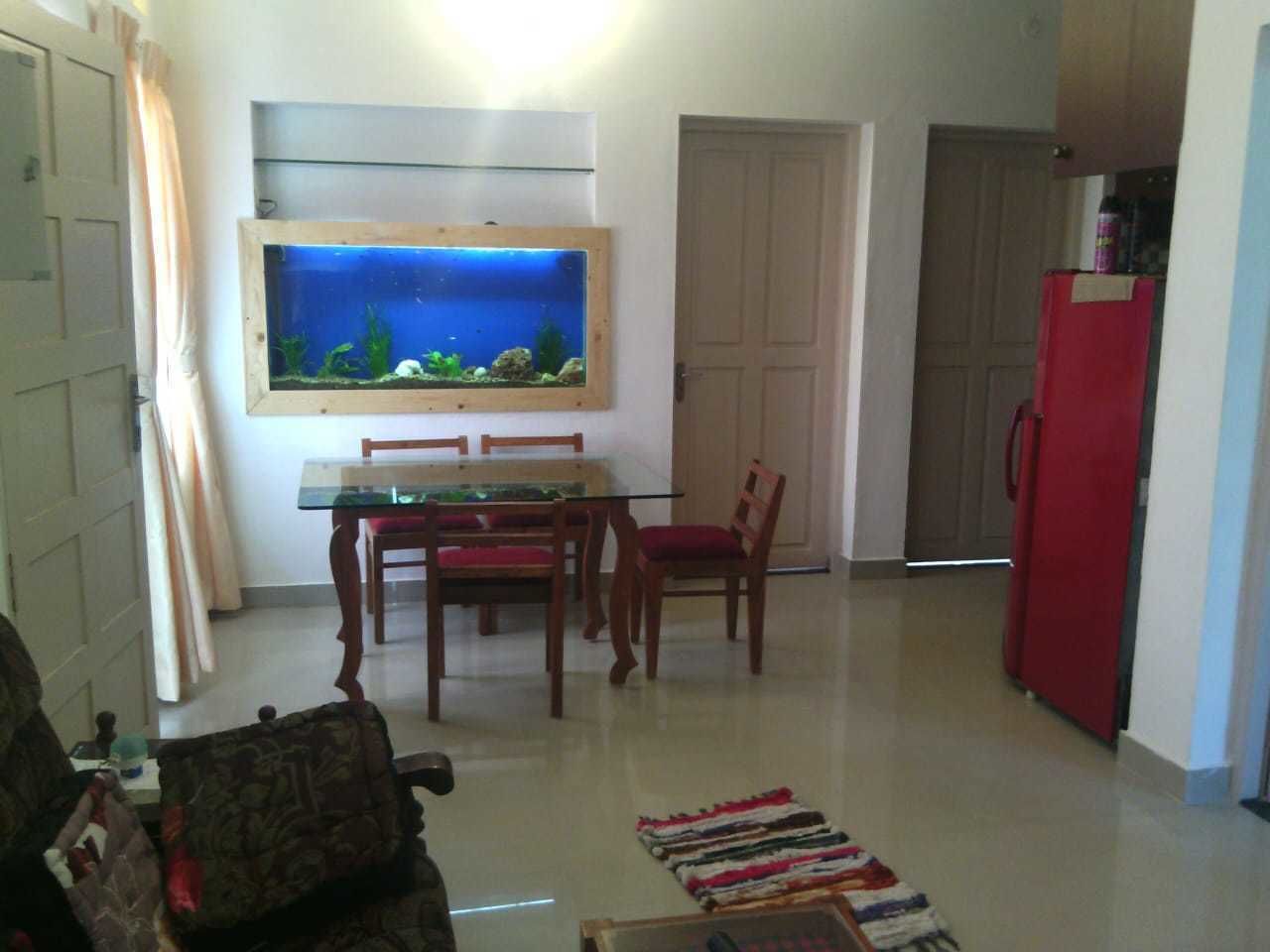 A living room with a dining table, chairs, a red refrigerator, and a large fish tank on the wall.