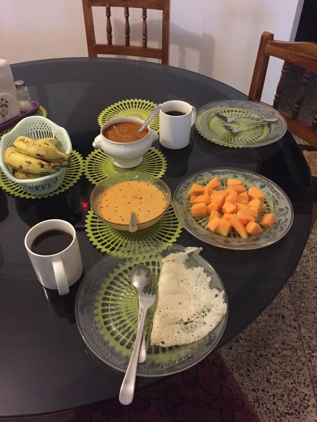 A round dining table with various dishes, including a bowl of soup, a plate of sliced vegetables, and a plate of rice.