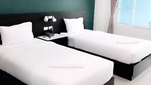 A hotel room with two single beds, a nightstand, a lamp, and a window with curtains. - Trang Grand Mansion (Trang)