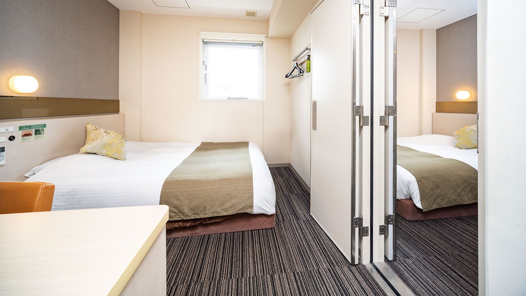 A hotel room with two beds, a desk, a window, and a mirror.