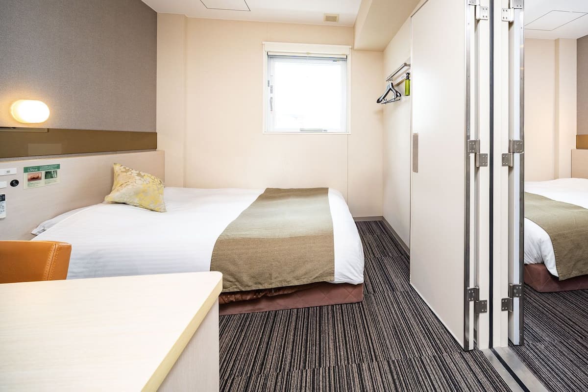 Une chambre d’hôtel avec deux lits, un bureau, une fenêtre et un miroir.