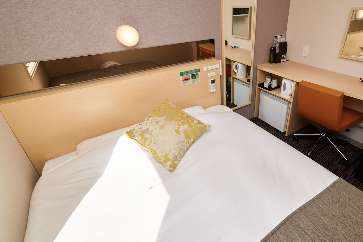 Une chambre d’hôtel équipée d’un lit, d’un bureau, d’une chaise, d’un miroir et d’une petite kitchenette.