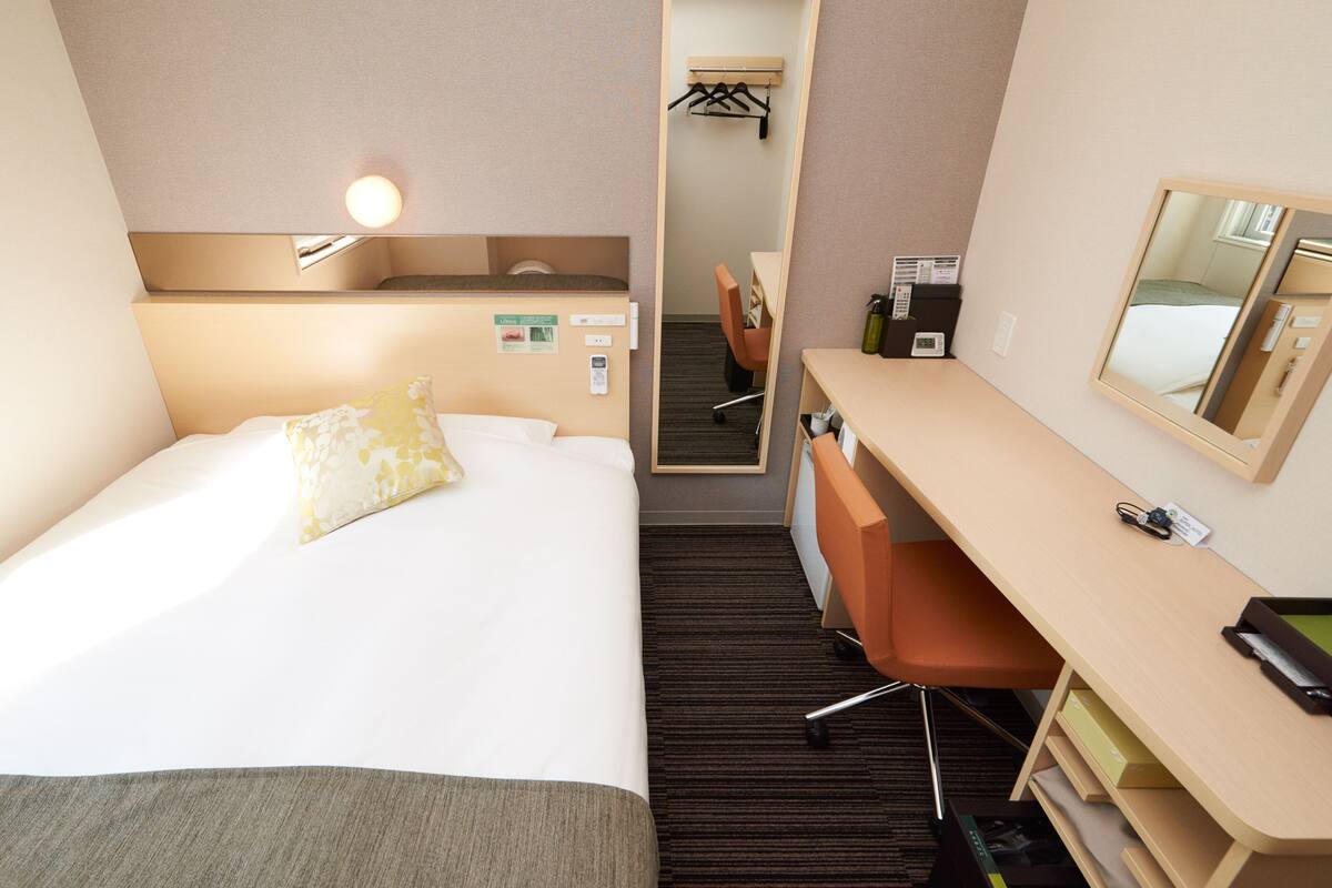 Une chambre d’hôtel équipée d’un lit, d’un bureau, d’une chaise, d’un miroir et d’une petite kitchenette.