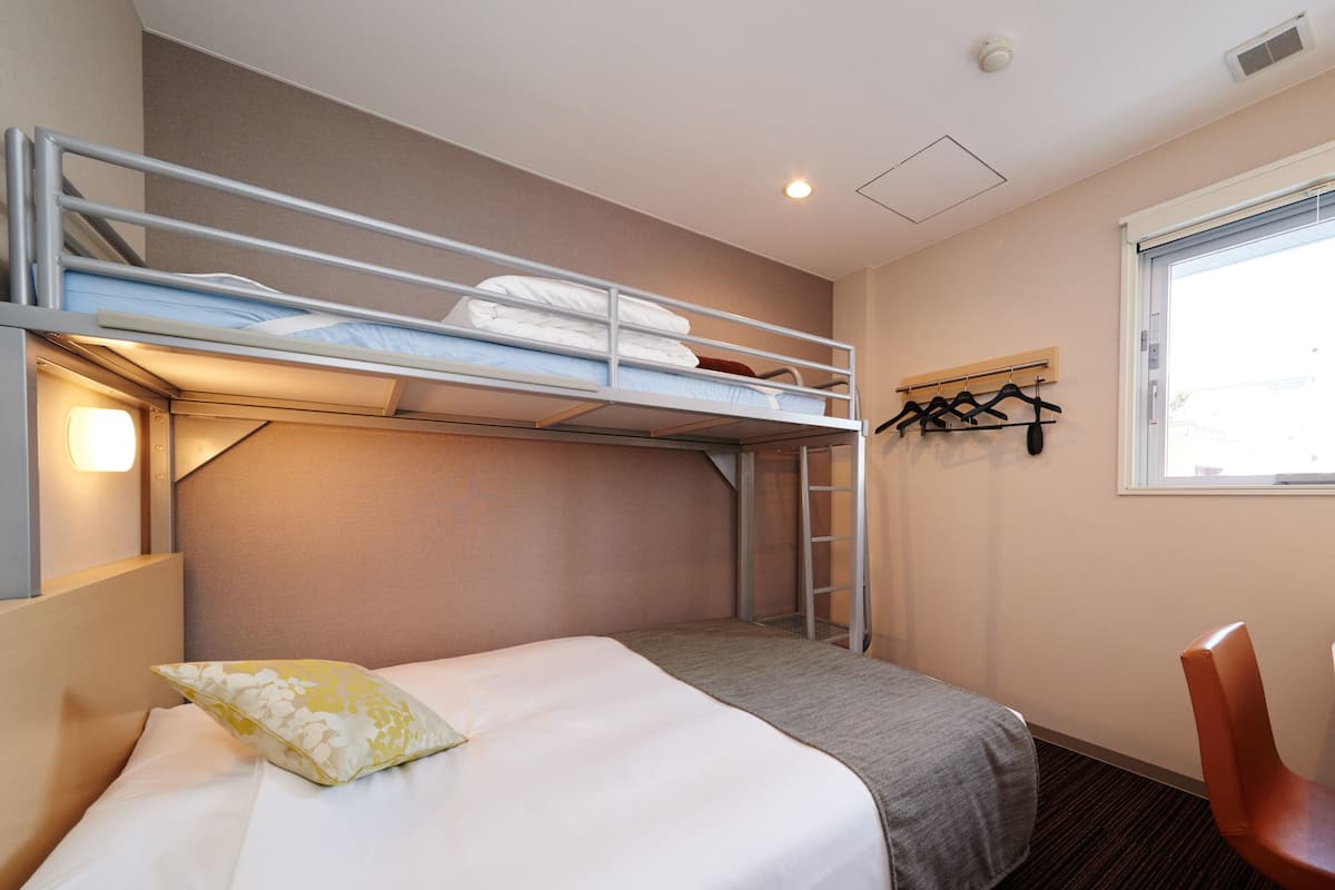 Une chambre avec un lit superposé, un bureau et une chaise, une fenêtre et un porte-manteau.