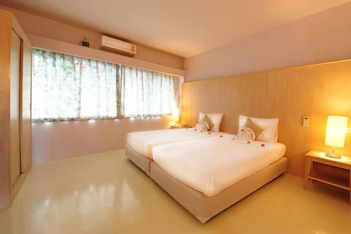 A double bed with a wooden headboard, a bedside table with a lamp, and a window with curtains.
