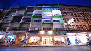 A multi-story hotel with balconies, a ground floor with shops, and a sign indicating room rates. - S2S Queen Trang Hotel (Trang)