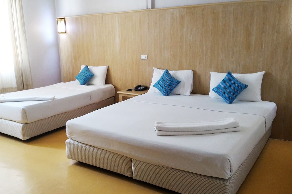 A hotel room with two beds, each with white linens and blue plaid pillows. There is a bedside table with a phone and a lamp.