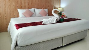 A hotel room with a wooden headboard, a neatly made bed with white bedding and pink pillows, a red throw blanket, a swan-shaped towel, a vase with flowers, and a bedside lamp. - S2S Queen Trang Hotel (Trang)