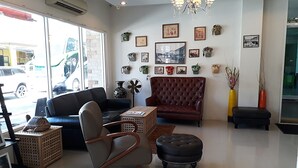 A modern living room with a sofa, armchair, ottoman, and a red armchair. There are several framed pictures on the wall and a chandelier. - S2S Queen Trang Hotel (Trang)