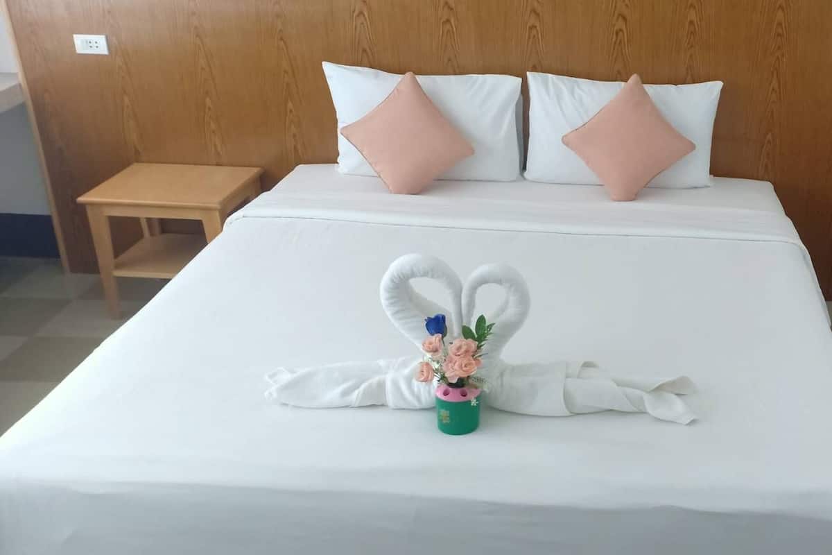 A neatly made bed with a towel and a small flower arrangement on the bedspread.