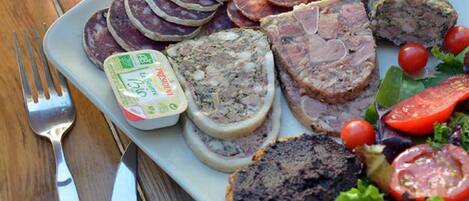 Un plato con diversas carnes, una bebida en un vaso y una baguette sobre una mesa de madera.