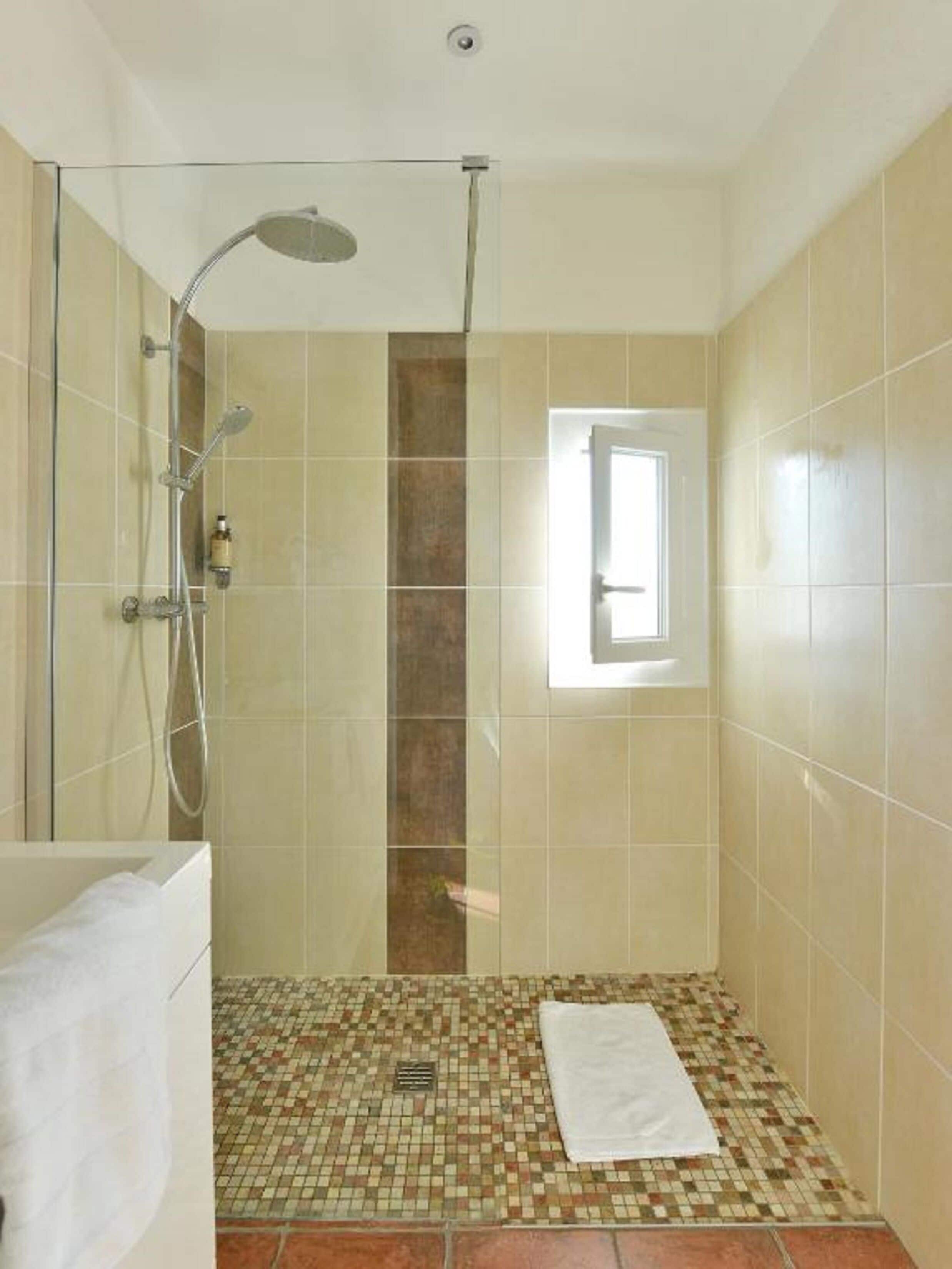 A shower with a glass door, a window, and a tiled floor.