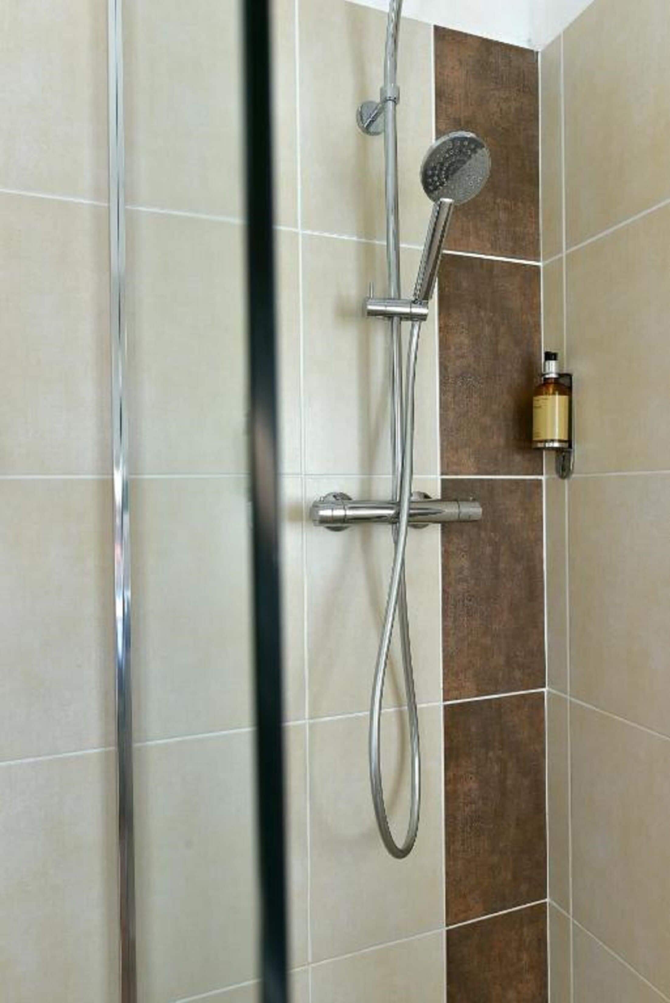 A shower with a handheld showerhead and a wall-mounted control panel.