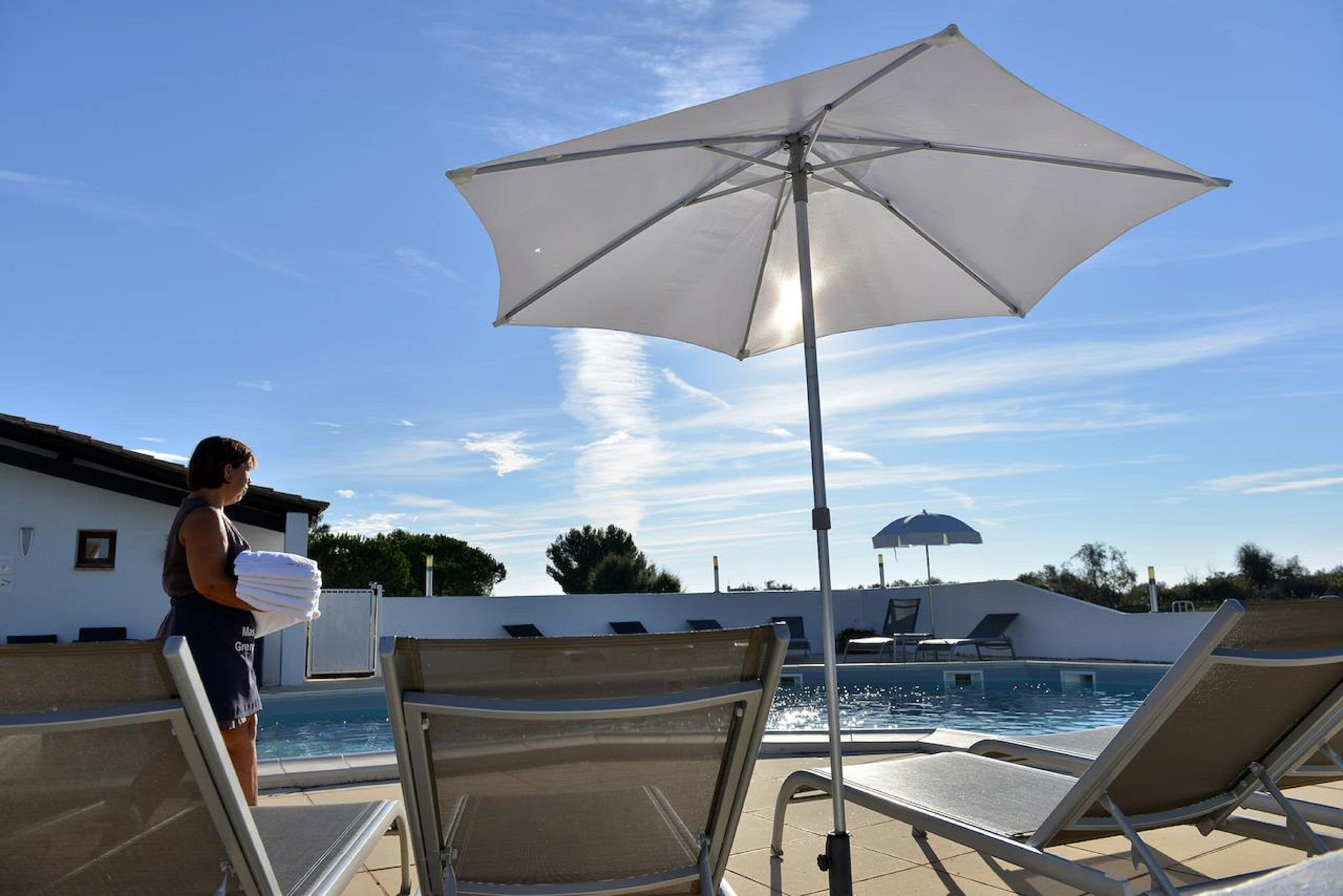 Una zona junto a la piscina con sillones de descanso y una sombrilla grande.