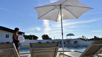 Una zona junto a la piscina con sillones de descanso y una sombrilla grande.