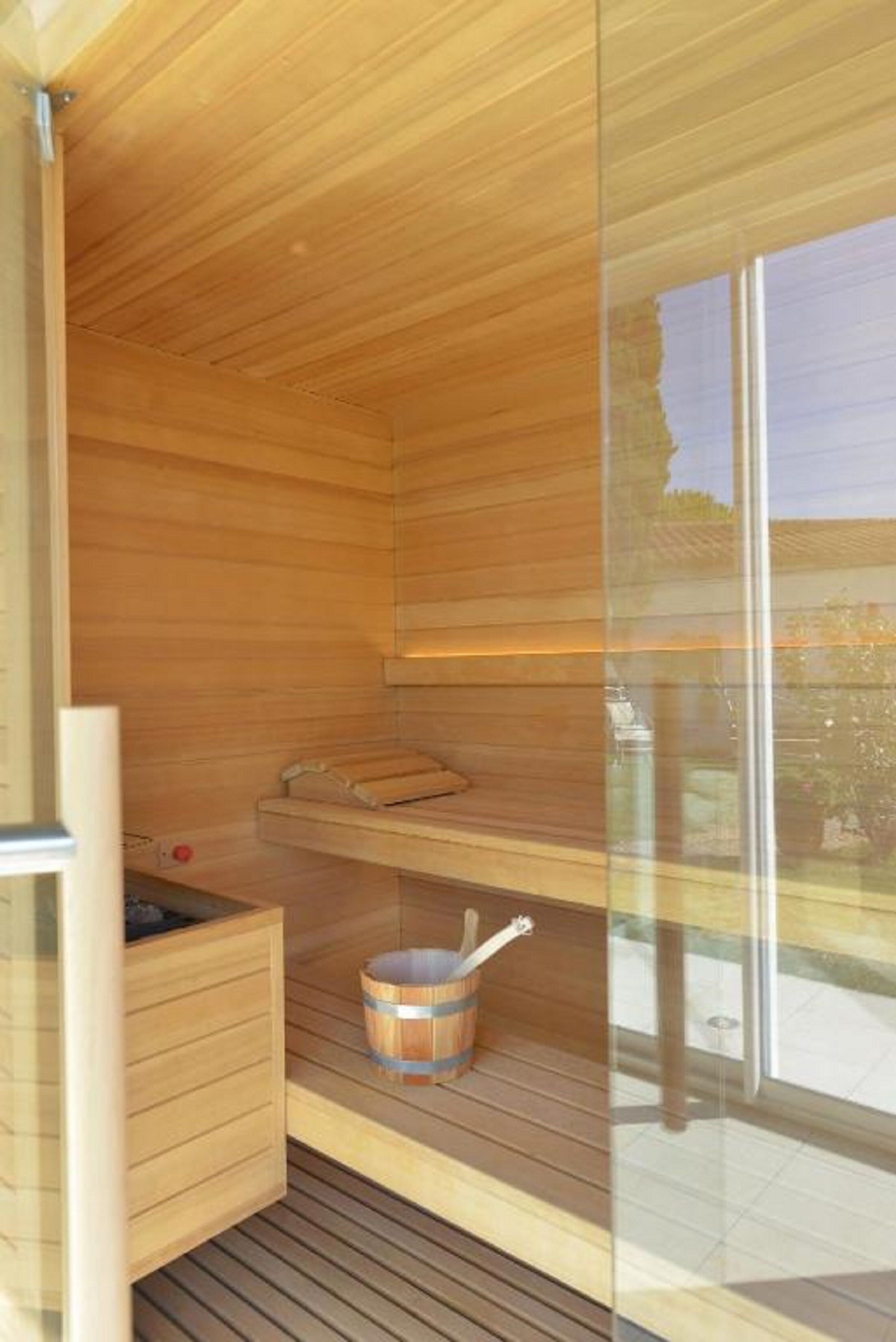 Een sauna met houten wanden en een glazen deur, een houten bank en een emmer.