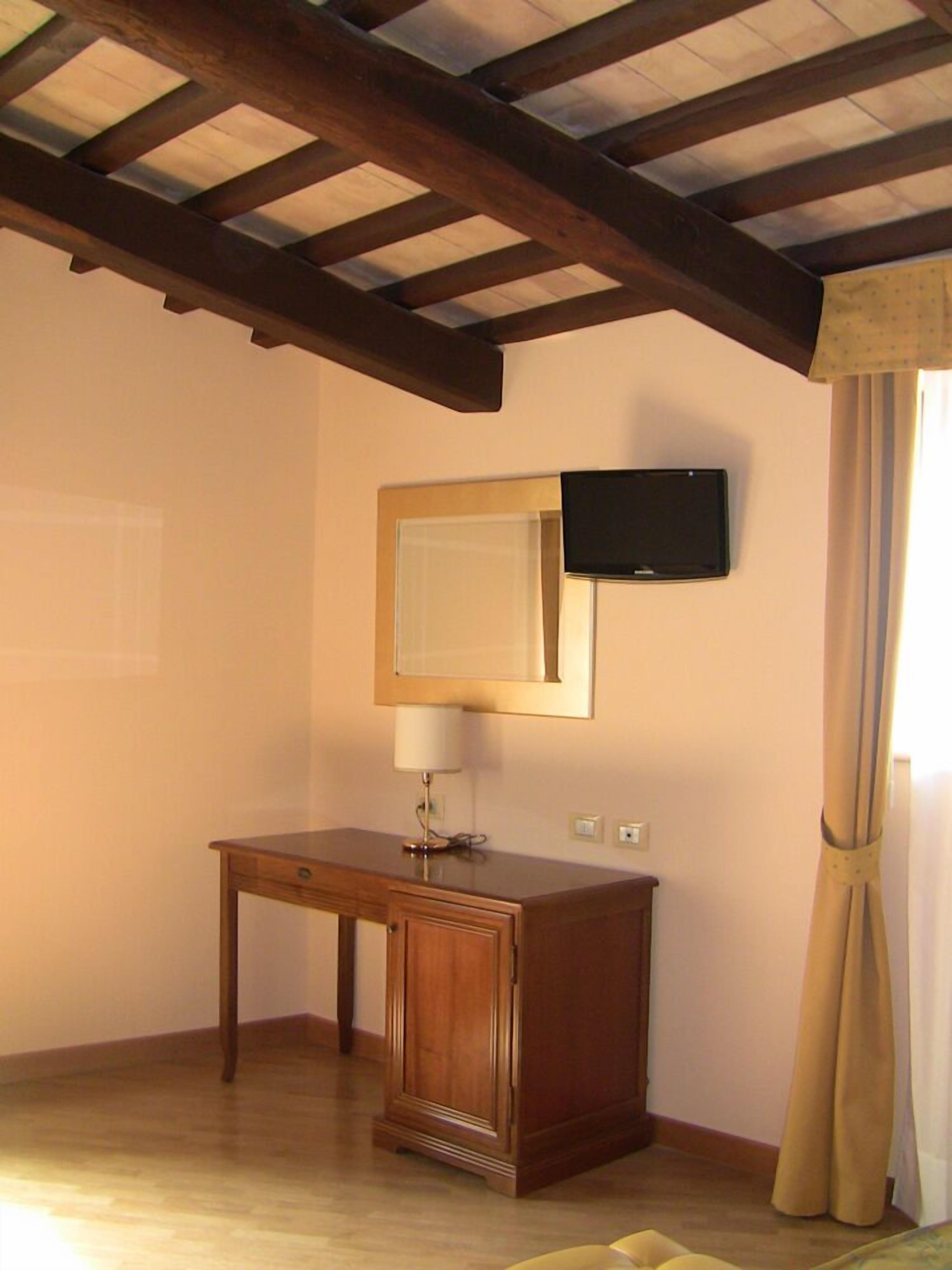 A room with a wooden desk, a wall-mounted TV, and a window with curtains.