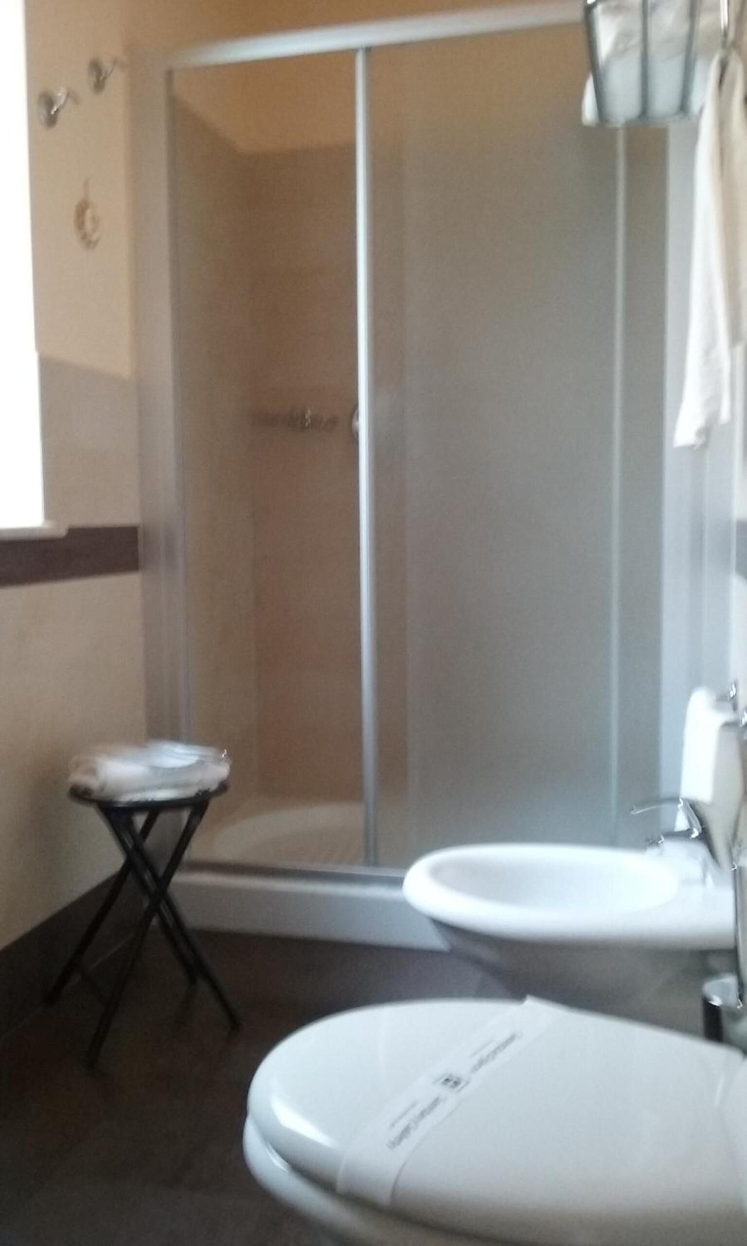 Een badkamer met een douchecabine van glas, een klein tafeltje en twee wastafels.