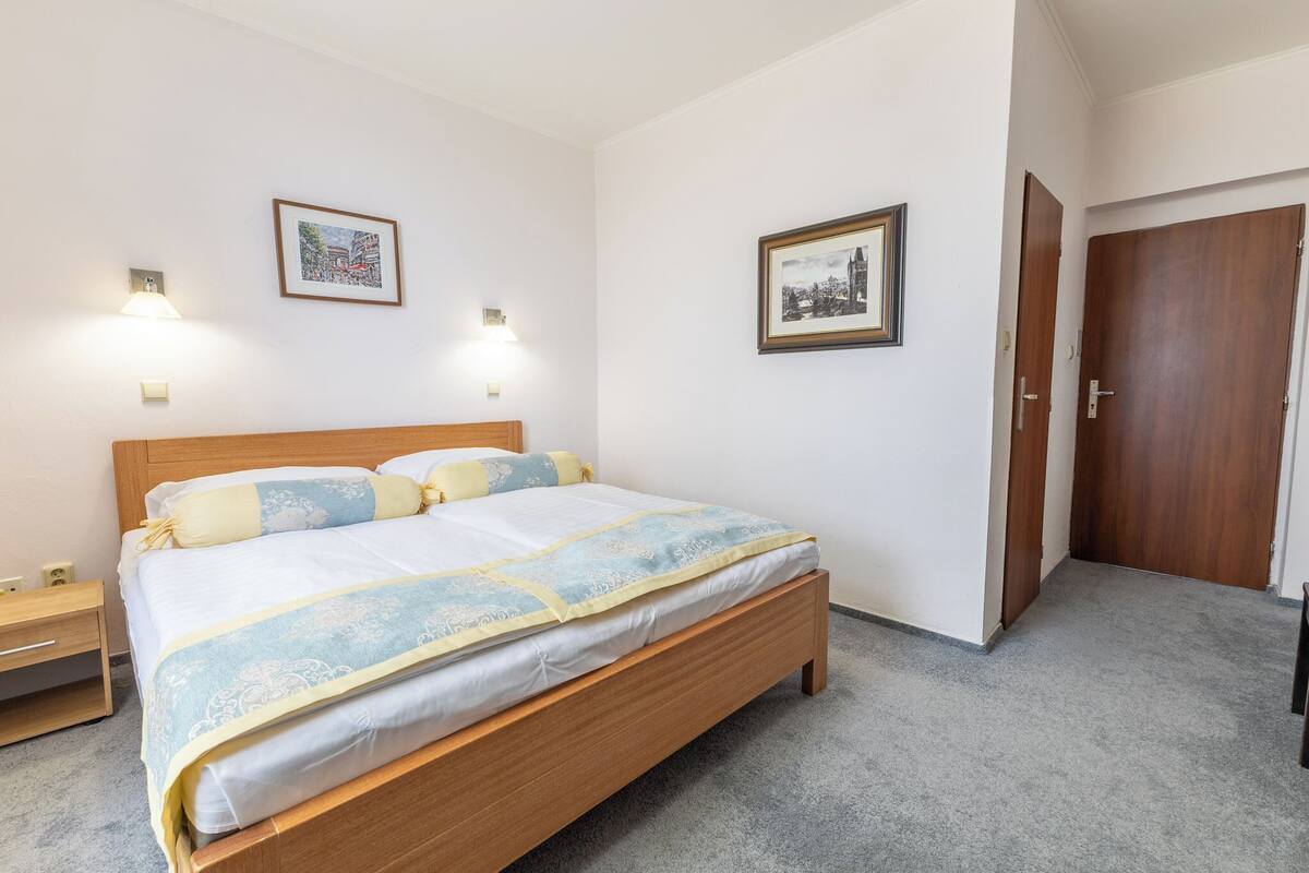 Uma cama bem arrumada com estrutura de madeira, duas mesas de cabeceira e duas luminárias fixadas na parede.