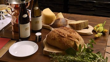 A wooden table with a bottle of wine, a cheese wheel, a loaf of bread, and some herbs.