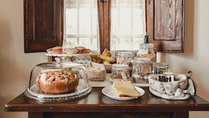 Une table sur laquelle on trouve divers aliments, notamment un pain, un panier de fruits et plusieurs pots de confitures.