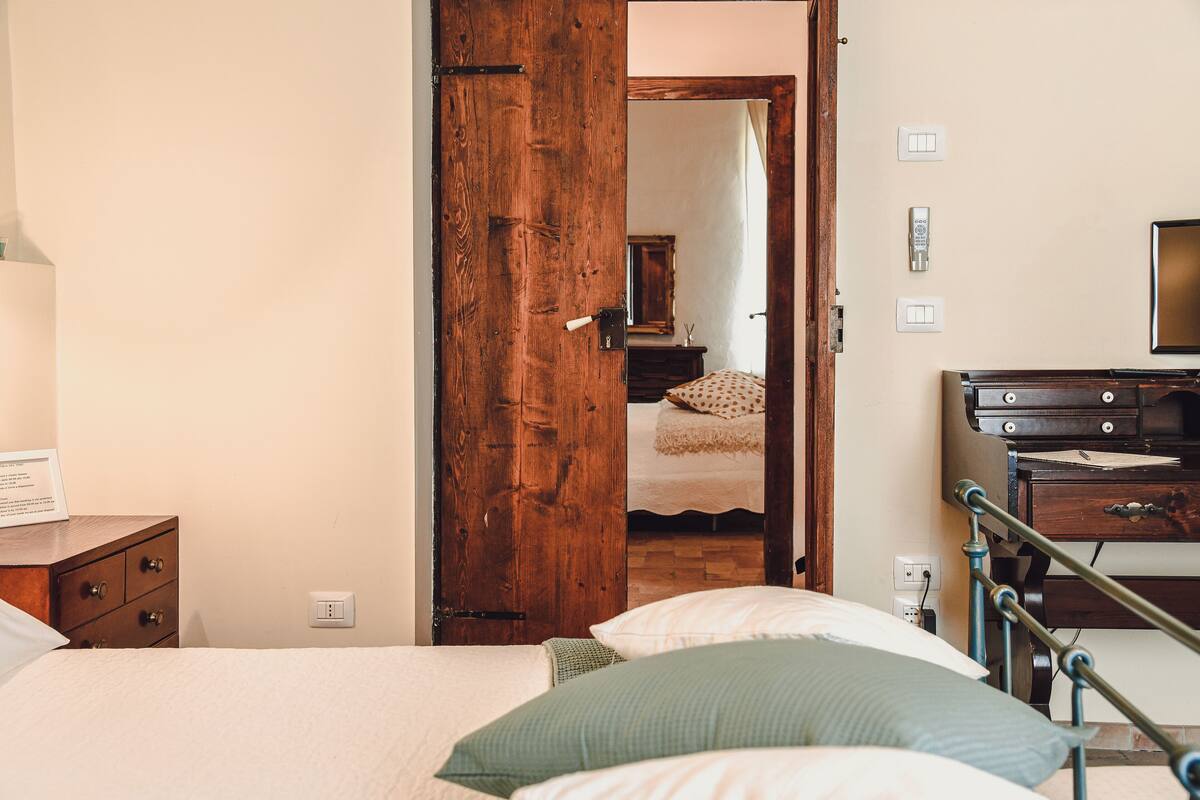 A bedroom with a wooden door, a bed with pillows, a dresser, and a mirror on the wall.