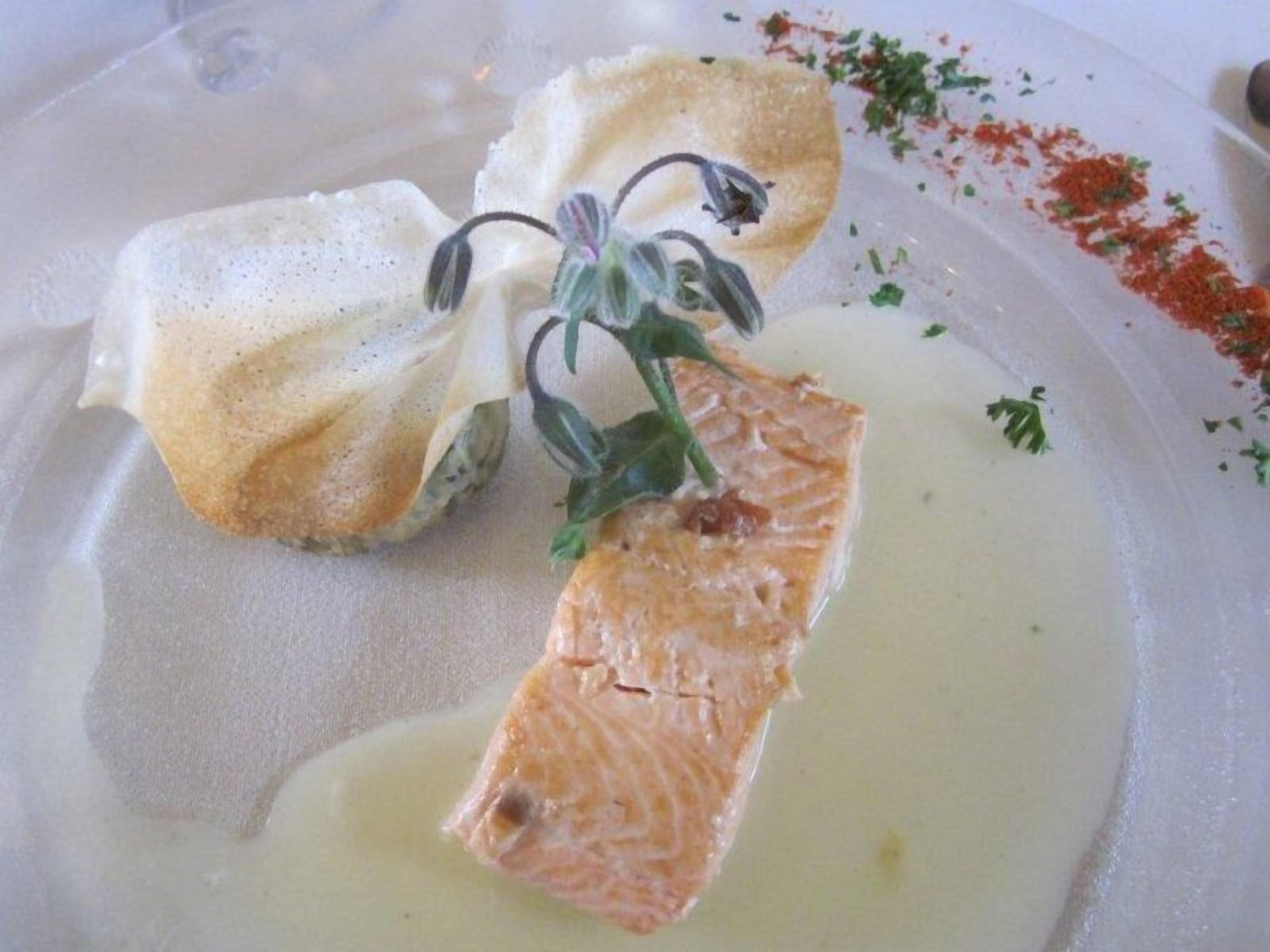 Une assiette avec du saumon, une fleur et quelques herbes aromatiques.