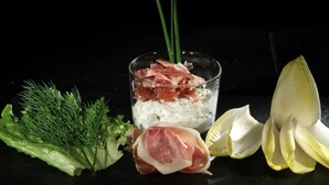 A glass with layered food items, including a green vegetable, a yellow fruit, and a red meat. - Hôtel Saint Martin (Gouvy)