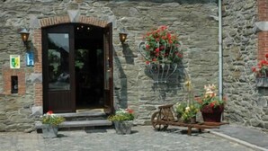 A stone building with a wooden door and steps leading up to it. There are potted plants and a bicycle outside. - Hôtel Saint Martin (Gouvy)