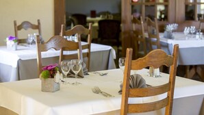 A dining area with wooden chairs and tables set for a meal, featuring a vase with flowers and wine glasses. - Hôtel Saint Martin (Gouvy)