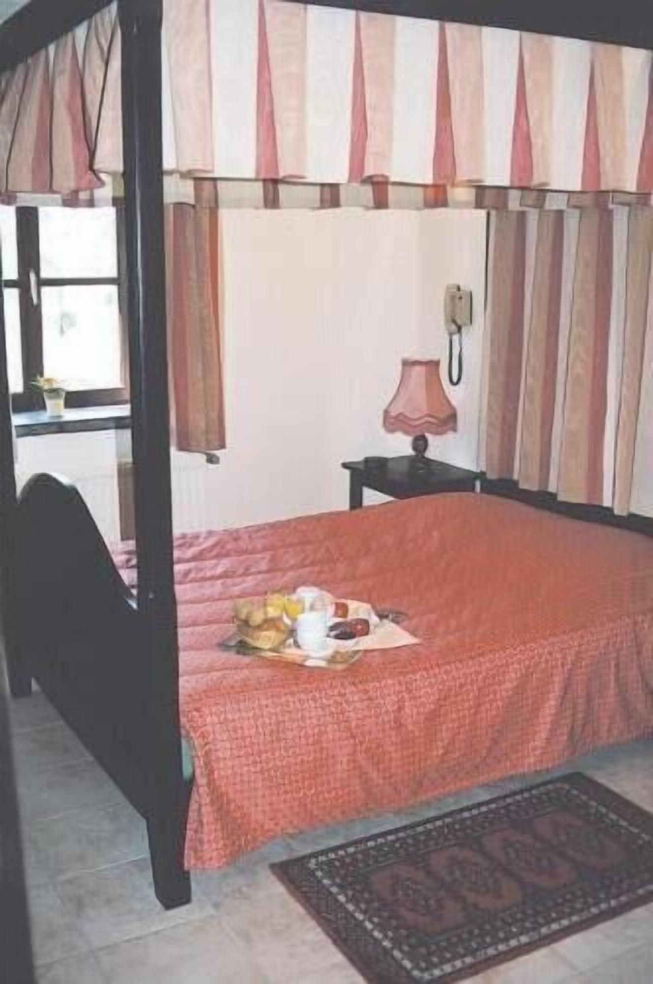 Un dormitorio con cama con dosel, una mesita de noche con lámpara y una ventana con cortinas.