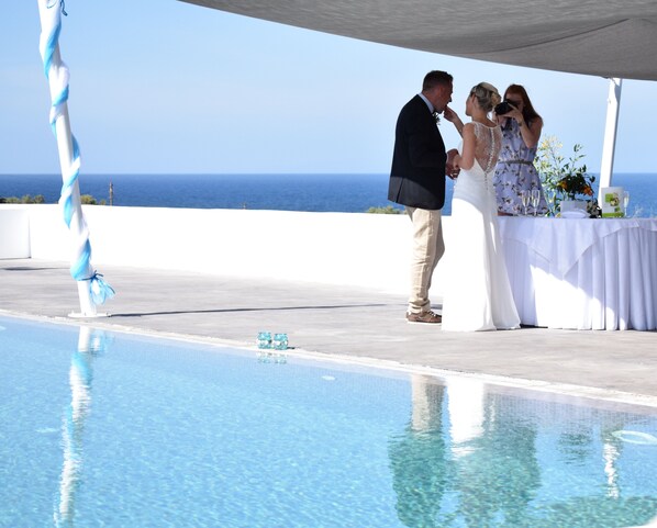 A wedding ceremony by a pool with a clear view of the ocean. - Sea and Sand Luxury Villas (Santorini)