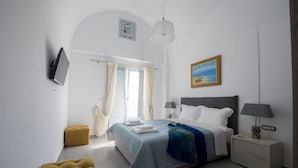 A modern bedroom with a bed, bedside tables, a TV, and a painting. - Sea and Sand Luxury Villas (Santorini)