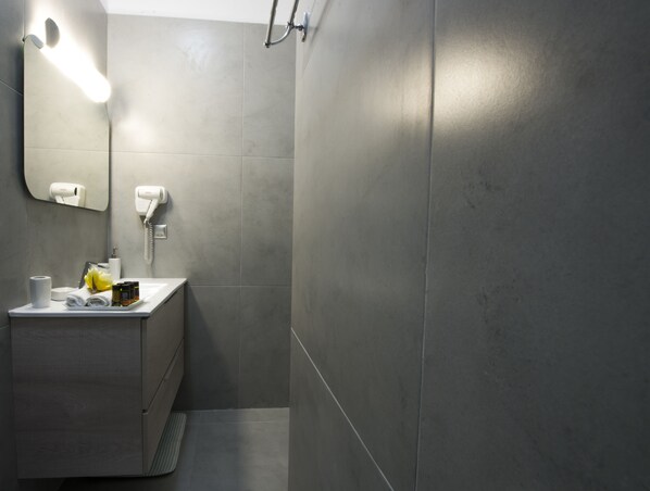 Une salle de bain moderne avec un mur recouvert de carreaux gris, un lavabo blanc avec des articles de toilette, un miroir et un sèche-cheveux.