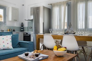 Uma cozinha moderna com geladeira de aço inoxidável, uma área de refeições com mesa de madeira e um sofá azul com almofada estampada de poá.