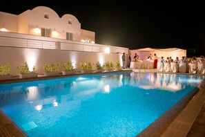 A swimming pool with a white building in the background. - Sea and Sand Luxury Villas (Santorini)
