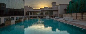 Piscina com vista para edifícios modernos e um pôr do sol ao fundo.