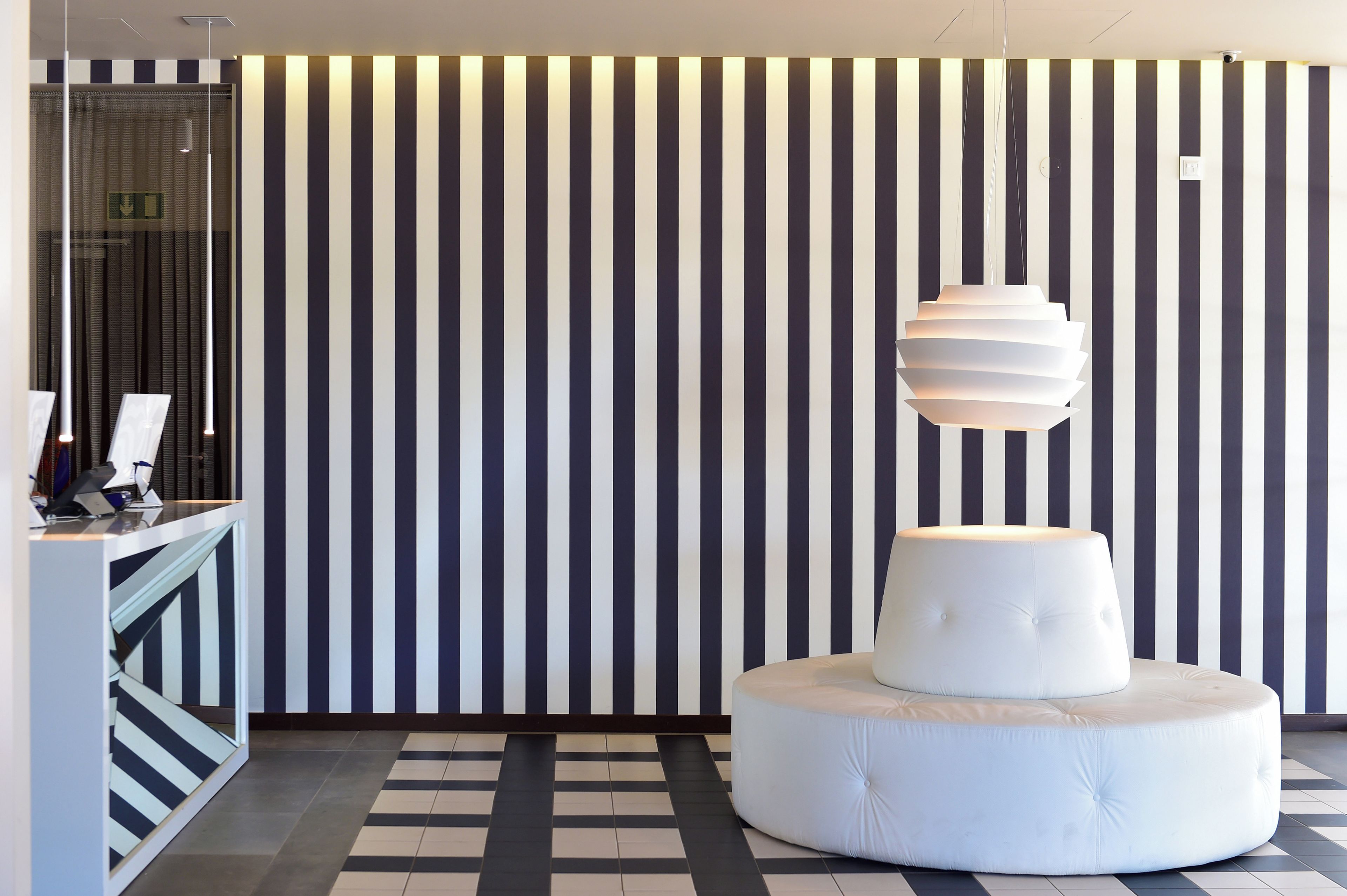 A modern interior with a striped wall, a round white ottoman, and a hanging light fixture.