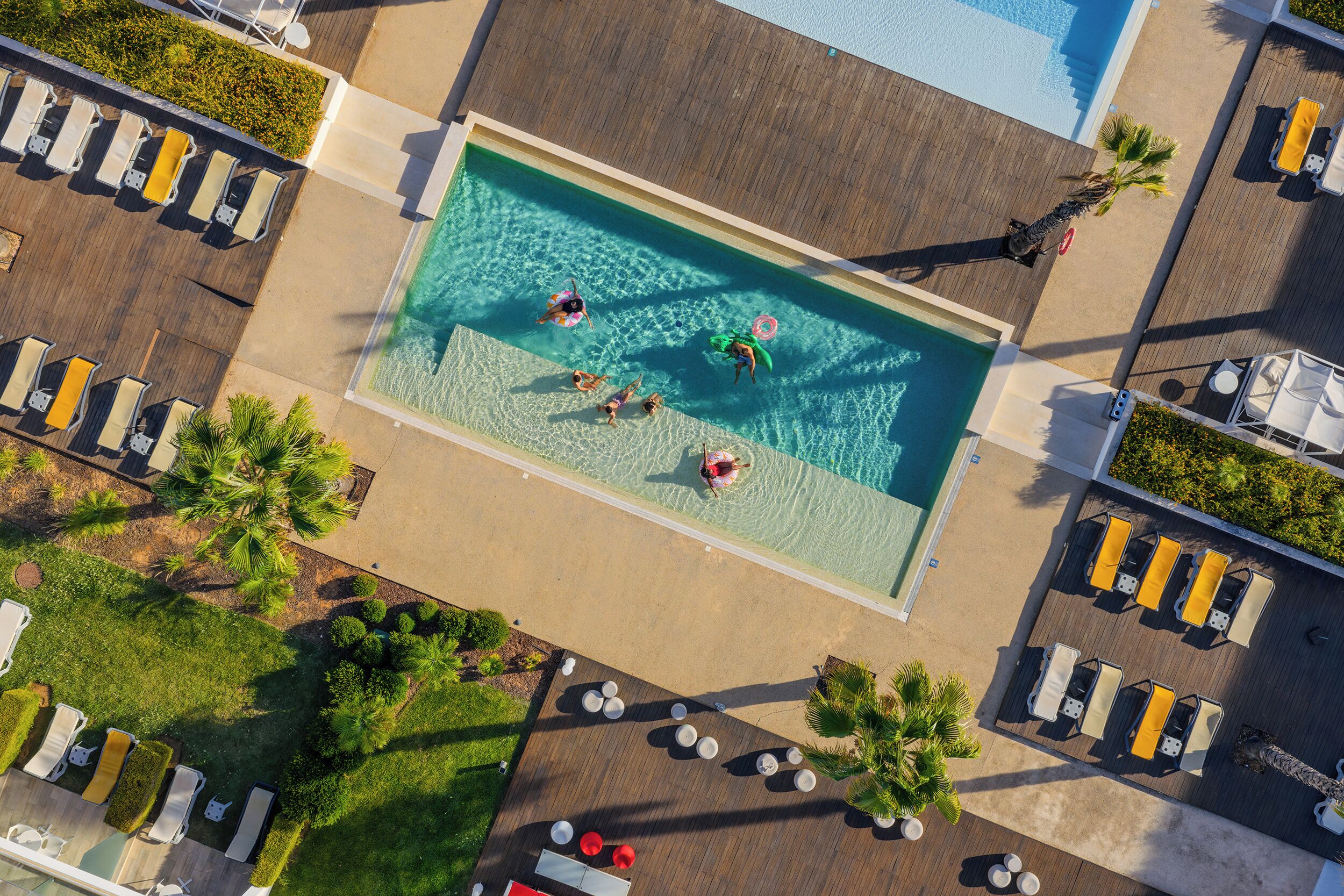An aerial view of a swimming pool surrounded by lounge chairs and palm trees.
