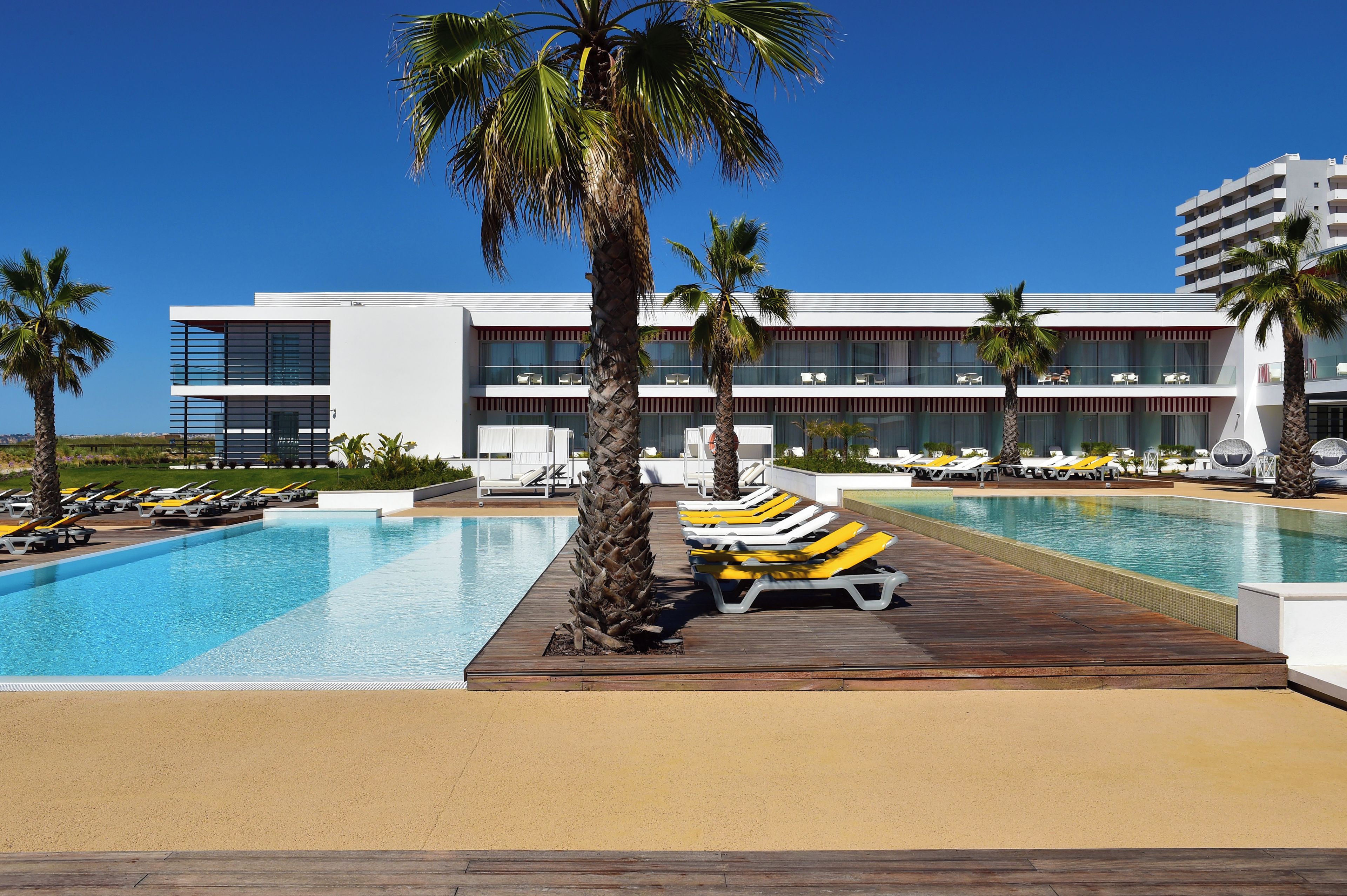 Un hotel moderno con piscina, tumbonas y palmeras.