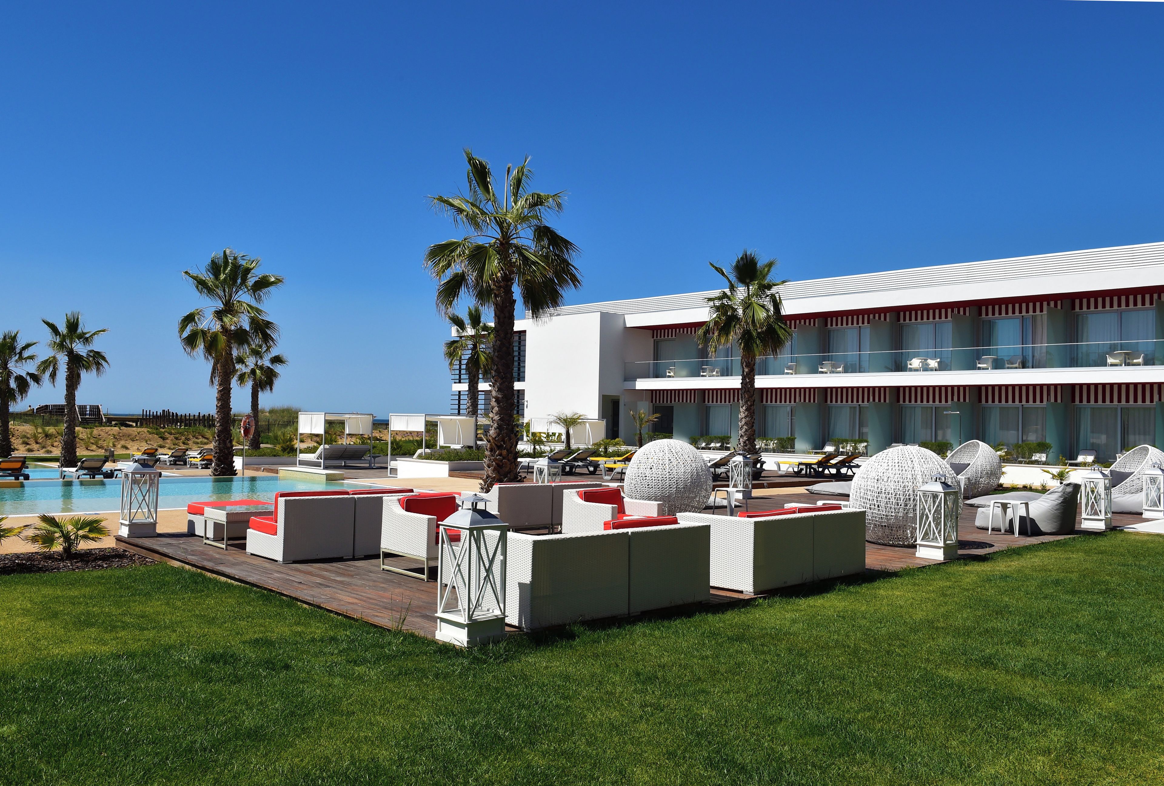 A poolside area with lounge chairs and a modern building with balconies.