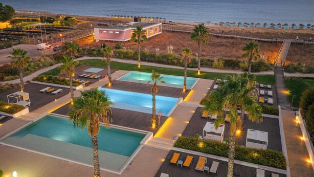 Een resort met meerdere zwembaden, palmbomen en strandparasols.