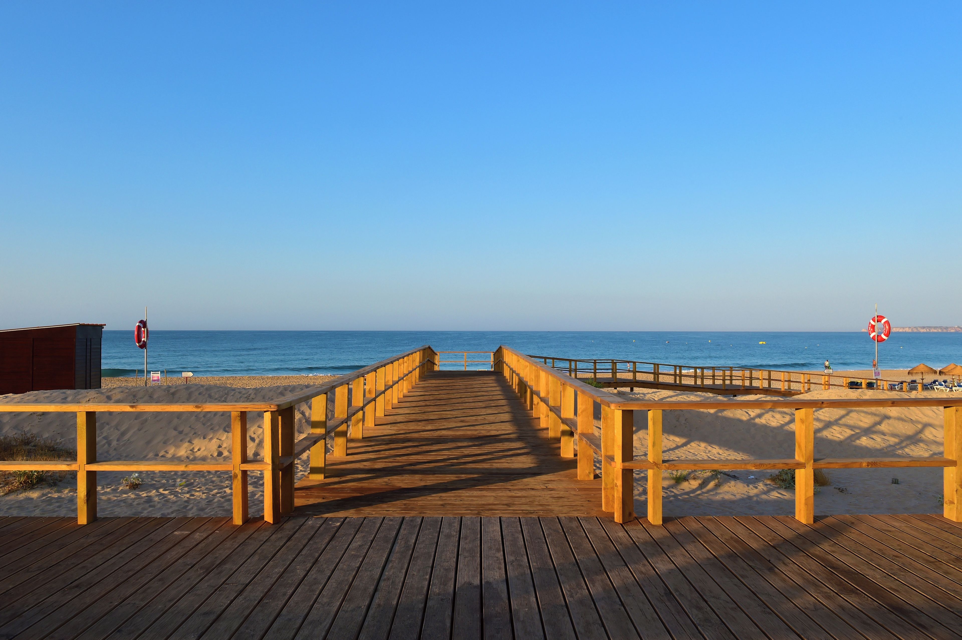 Una pasarela de madera que conduce a una playa, con un letrero de boya salvavidas y un letrero de prohibido bañarse.