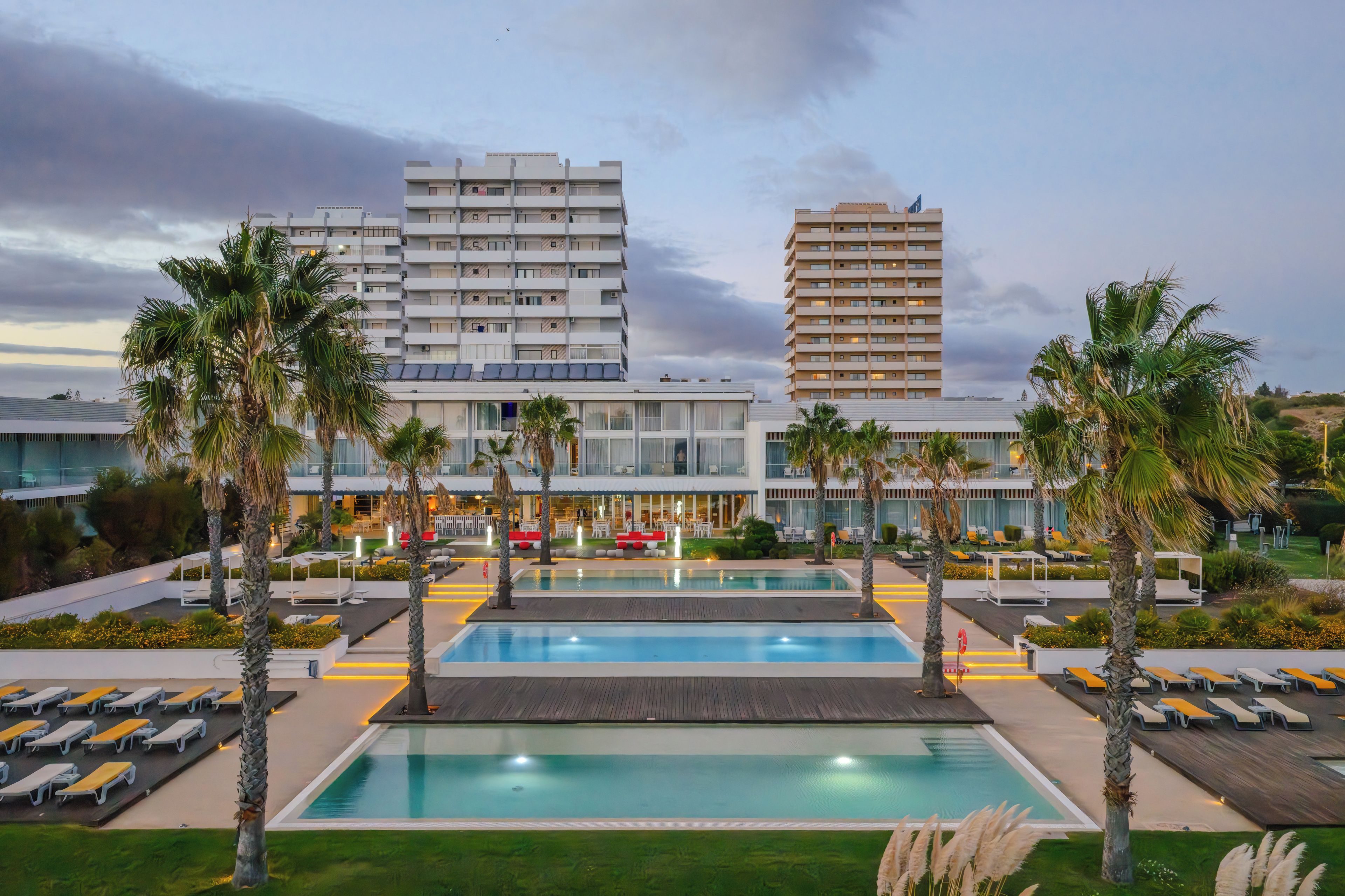 A hotel with multiple swimming pools, palm trees, and modern architecture.
