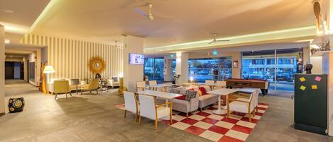 A modern hotel lobby with a checkered floor, seating area, and a pool table.