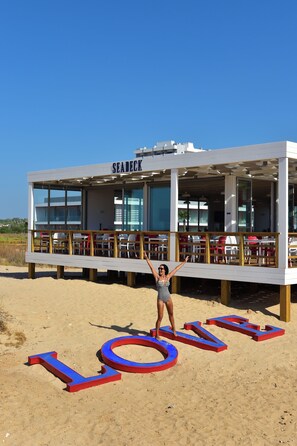 Un restaurant situé en bord de mer, appelé « SEA DECK », avec une terrasse et une zone sablonneuse devant l’établissement.